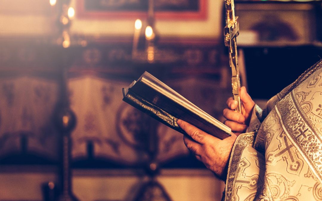 Priest praying in the church holding holly bible and cross