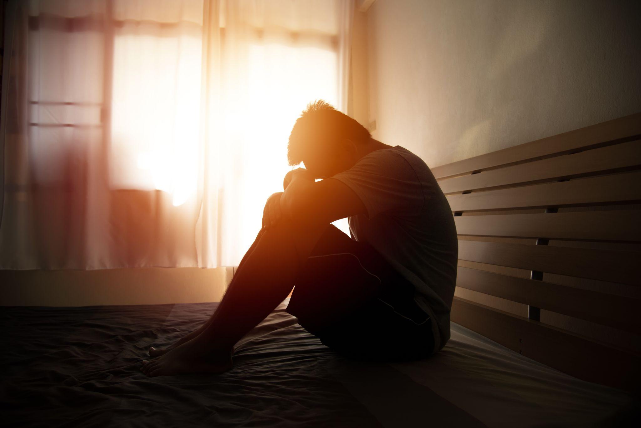 Desperate man in silhouette sitting on the bed with hands on head